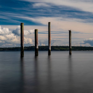 Wooden posts in lake against sky