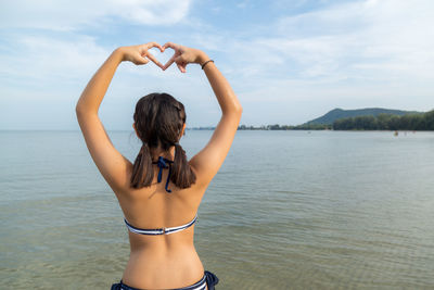 Rear view of woman standing in sea against sky