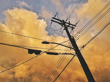 Low angle view of electricity pylon against cloudy sky