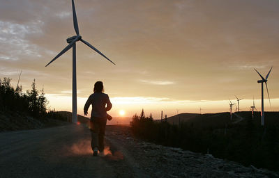 Man standing by traditional windmill against sky during sunset