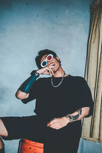 Young woman wearing sunglasses standing against wall