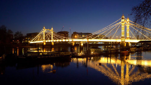 Illuminated bridge over river against sky at night