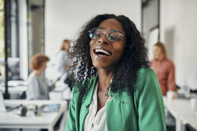 Portrait of a laughing businesswoman in office with colleagues in background
