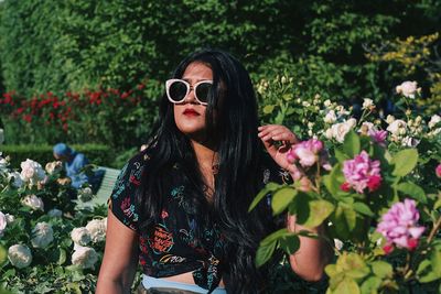 Young woman wearing sunglasses while standing amidst flowers at park