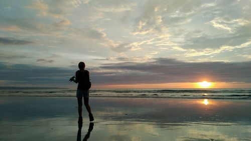 Full length of woman standing on beach against sky during sunset