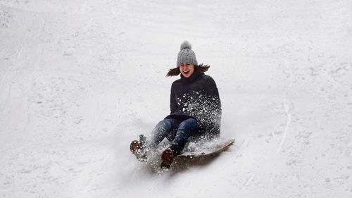 Full length of woman sledding on snow covered field