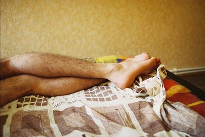 Low section of man sitting on bed at home