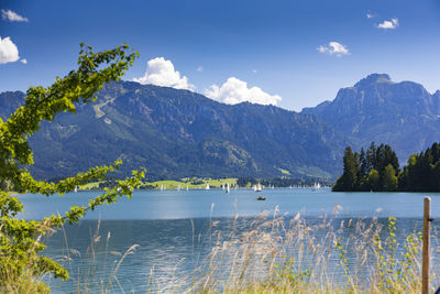 Scenic view of lake forggensee and rocky mountains against sky