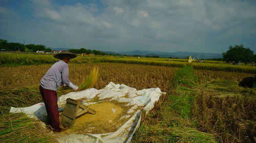 Farmer harvesting crops at farm against cloudy sky