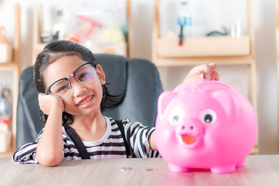 Portrait of girl putting coin in piggy bank at home