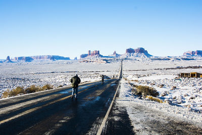 People on snow covered landscape against clear blue sky