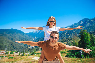 Portrait of happy young man with arms outstretched against mountain