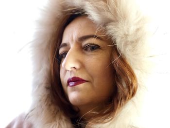 Close-up portrait of mature woman wearing fur coat against white background