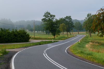 Empty road along trees and plants against sky