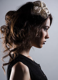 Side view of beautiful young woman wearing hair clip in brown hair against gray background