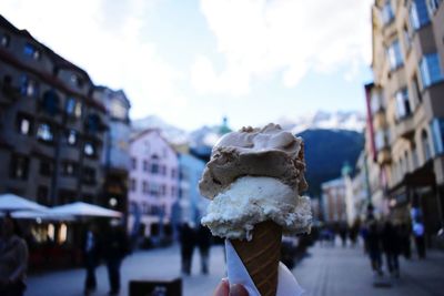 Close-up of person holding ice cream in city against sky