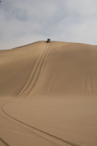 Distant view of off-road vehicle moving down sand dune against sky