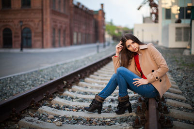Full length portrait of woman sitting on railroad track in city