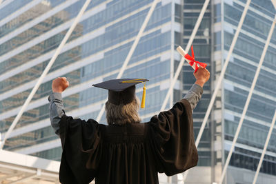 Rear view of man wearing graduation gown against building