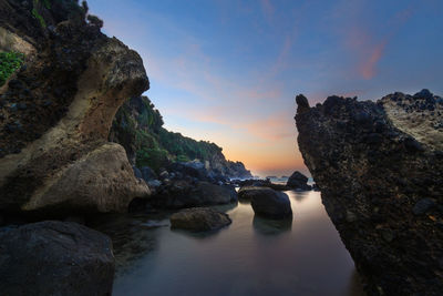 Rock formation amidst sea against sky during sunset