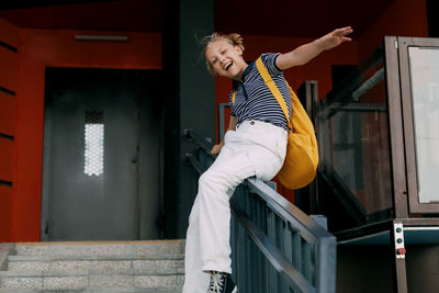 A teenage girl laughs and slides down the railing on her way to school. a cheerful girl hurries 