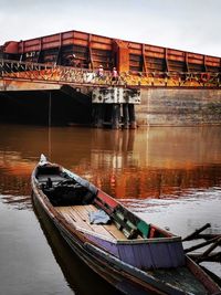 Boat moored on pier by river against sky