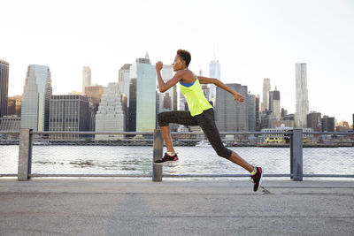 Athlete jumping on promenade by river against clear sky