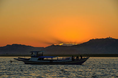 Boat on lake at sunset against orange sky