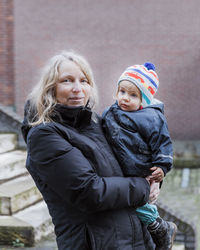 Portrait of grandmother carrying cute granddaughter while standing against wall