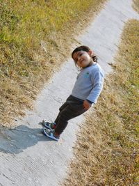 Cute girl looking away while standing on footpath amidst grassy field