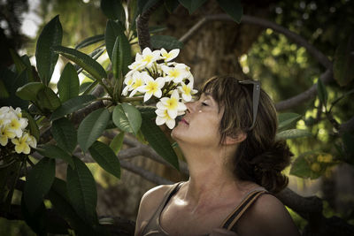 Close-up of woman smelling frangipani flower outdoors