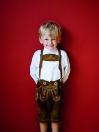Portrait of happy boy standing against red wall