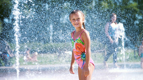 Happy girl of seven years, in swimsuit, having fun between water splashes in fountain . sunny