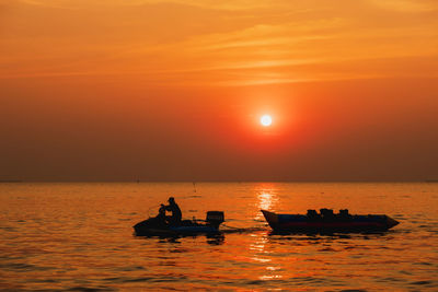 Silhouette boat in sea against orange sky