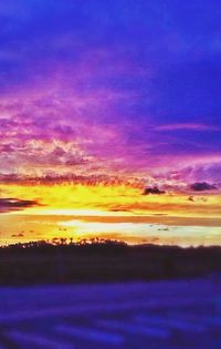 Scenic view of landscape against cloudy sky at sunset