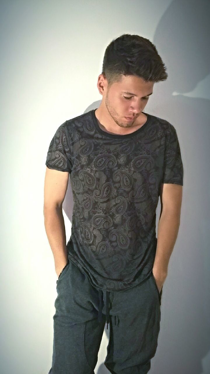 YOUNG MAN LOOKING AWAY WHILE STANDING ON WHITE WALL