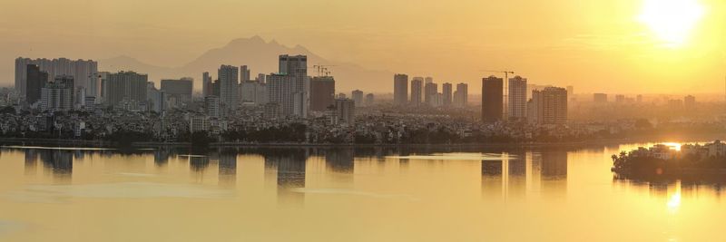 Scenic view of river by buildings against sky during sunset