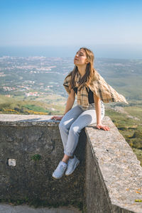 Side view of young woman standing against sky