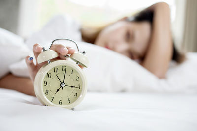 Young woman touching alarm clock while lying on bed at home