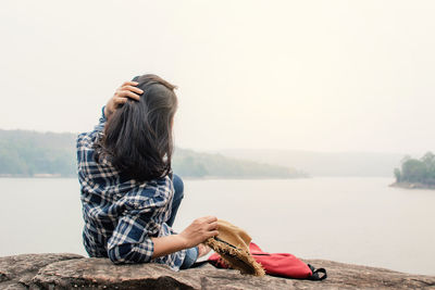 Young woman lying on rock by lake against clear sky