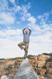 Full length of young man doing yoga on log against cloudy sky