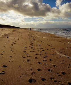 Footprints on sand at beach against sky