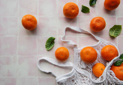 Mesh bag with oranges, tangerines on a pink tile background