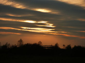 Silhouette trees on landscape against sky at sunset