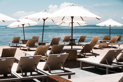 Chairs and tables on beach by sea against sky