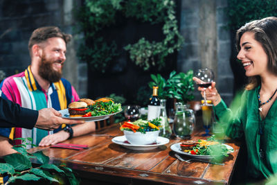 Cropped hand of waiter keeping food on table while young couple dating in restaurant