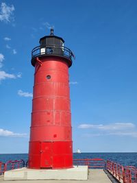 Lighthouse by sea against blue sky