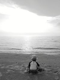 Rear view of man sitting at beach against sky