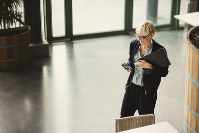 High angle view of businesswoman using smart phone while standing in creative office