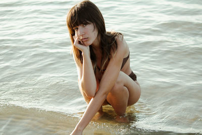 Young woman in water sitting in editorial pose